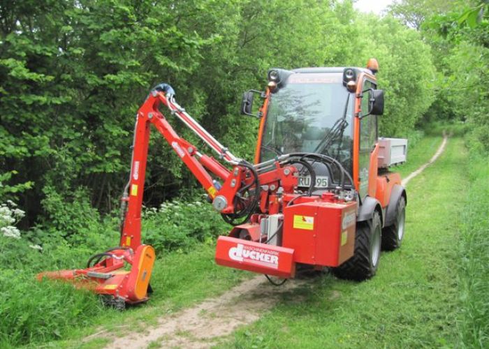 Großer roter Rasenmäher auf Feldweg schneidet Gras